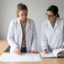 Two lab scientists reviewing a chromatogram printout and a maintenance logbook at a bench